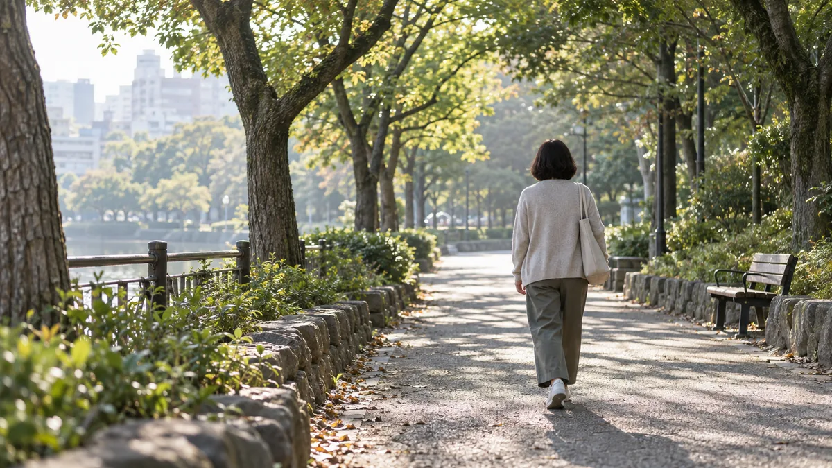 朝の公園の並木道を、ゆっくり歩く50代の女性の後ろ姿