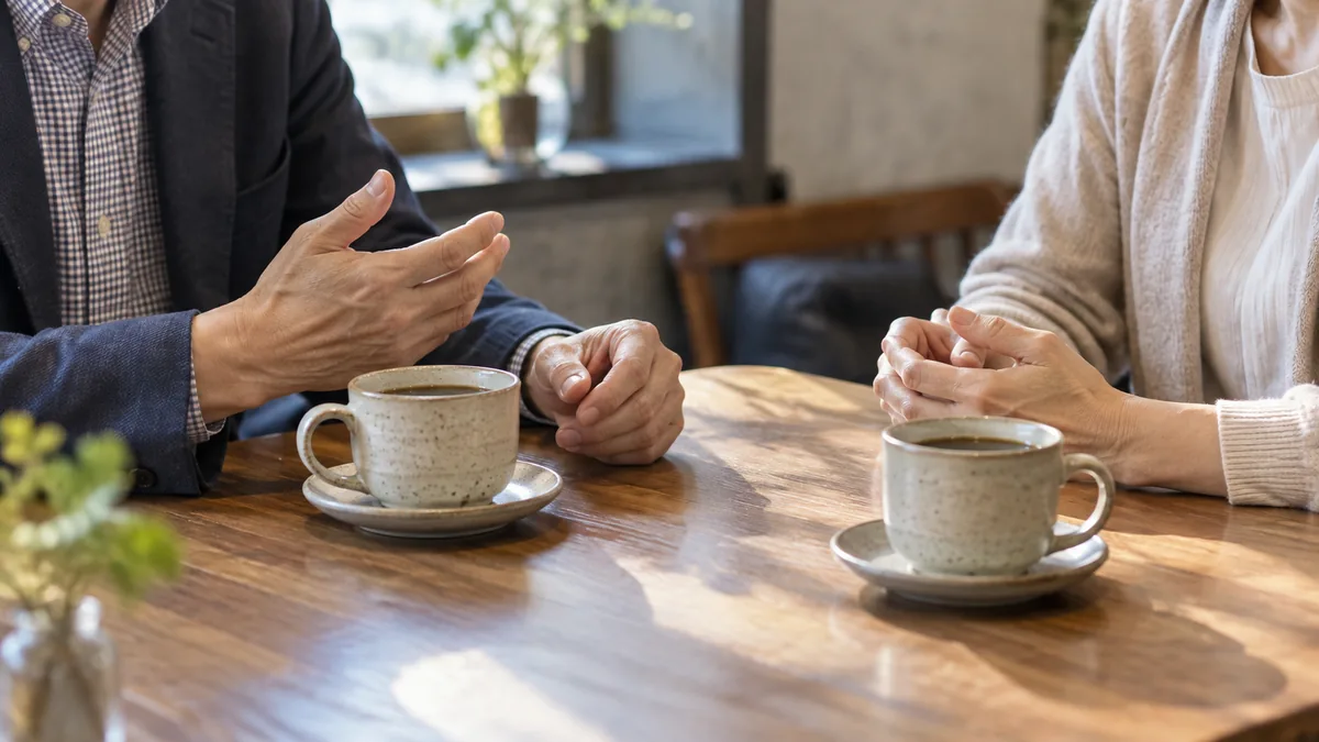 カフェで向かい合う50代の男女の手元と、2つのコーヒーカップ