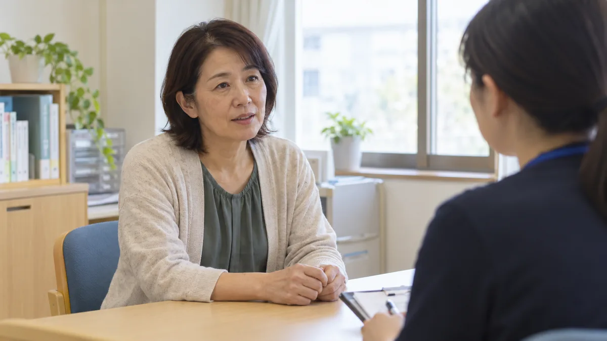 地域の相談窓口で、相談員と向かい合って話をする50代の女性