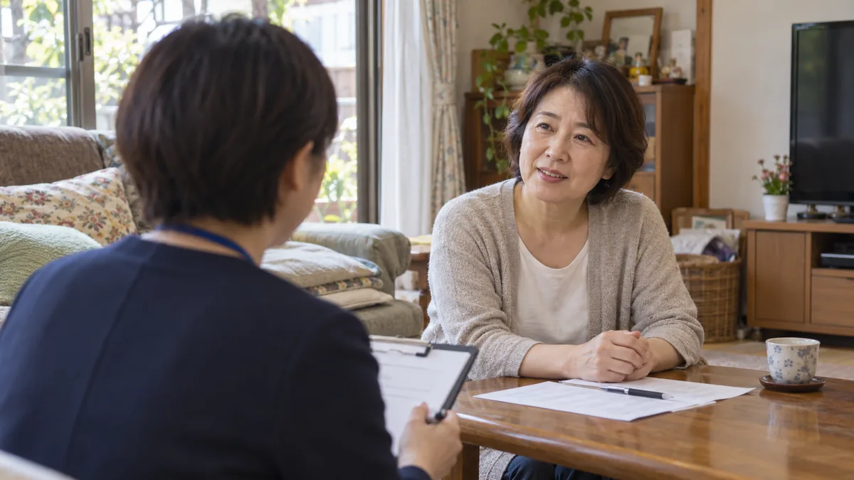 自宅のテーブルで、ケアマネジャーと書類を見ながら話す50代の女性（ケアマネジャーは後ろ姿）